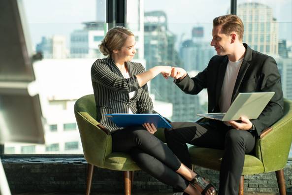 a man and woman sitting in chairs with laptops and papers